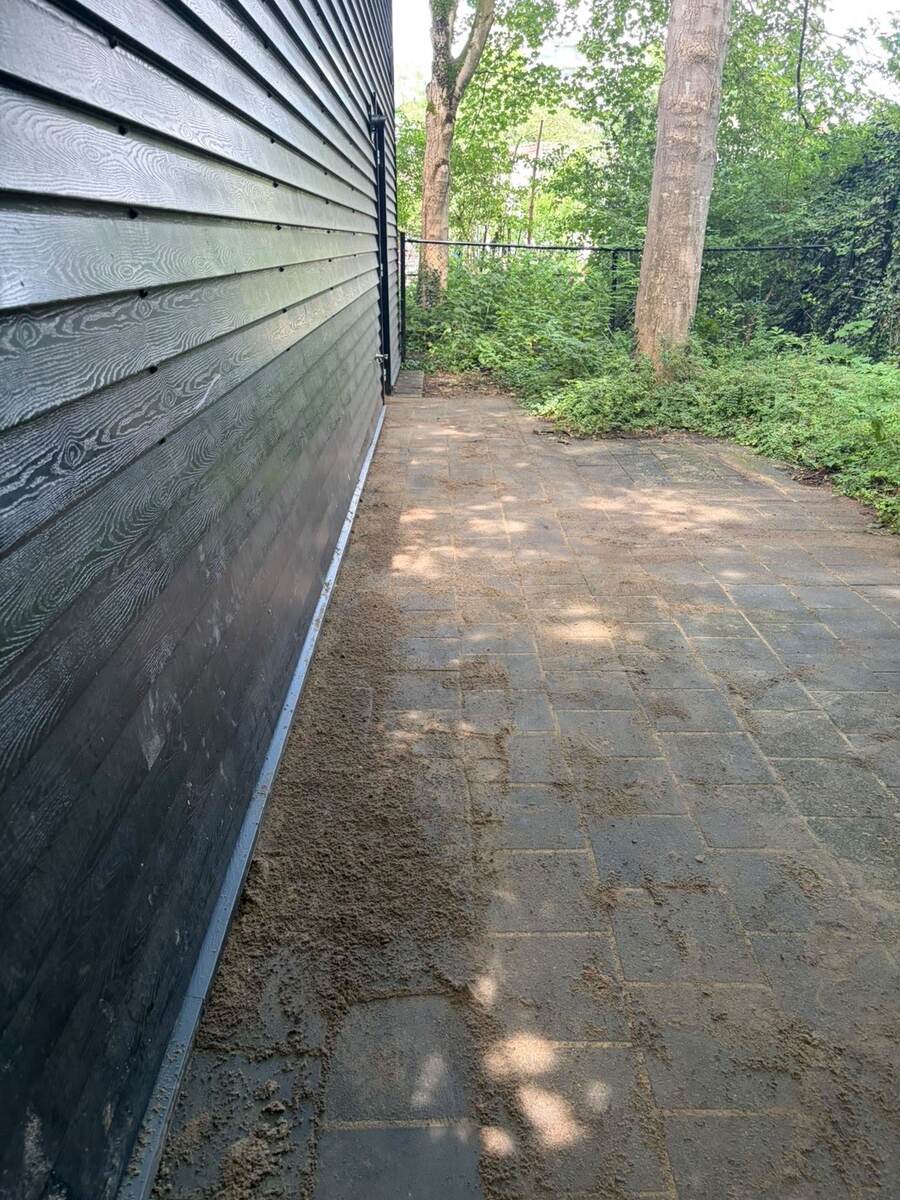 Teruggelegde bestrating met een strook zand langs de gevel na werk aan het riool