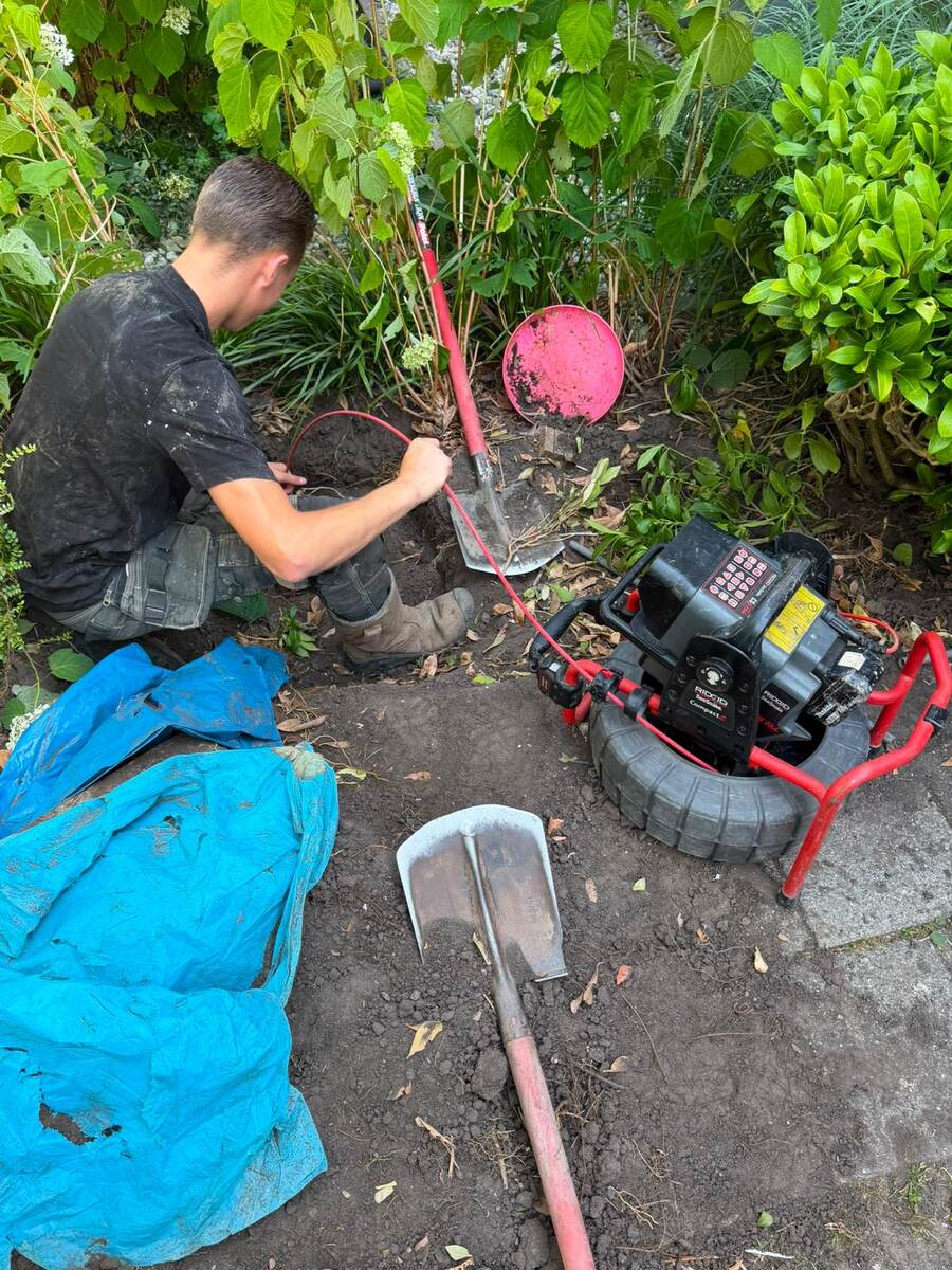 Monteur voert de spiraal van de ontstoppingsmachine in het riool bij een put in de tuin