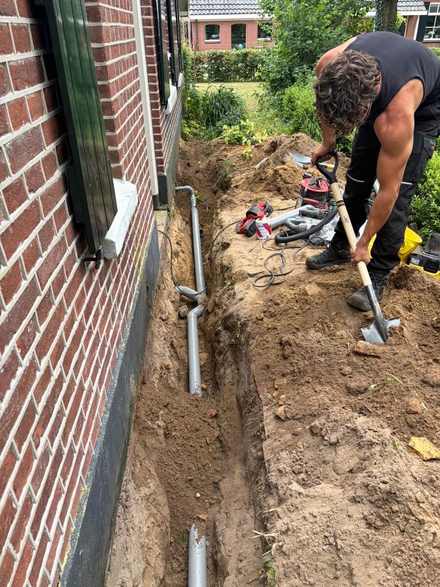 Monteur schept de sleuf dicht waarin de nieuwe riolering langs de woning ligt